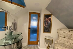 Een badkamer met een glazen wastafel, een houten deur en een lijst met een foto aan de muur.