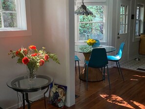 Un coin repas avec une table en verre, des chaises bleues et un vase rempli de fleurs rouges.