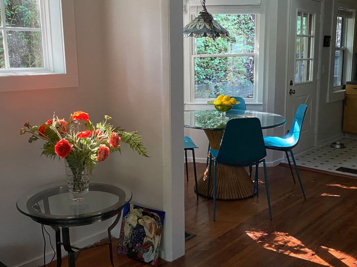 A dining area with a glass table, blue chairs, and a vase of red flowers.
