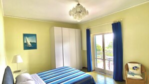 A bedroom with a bed, a chair, a window with curtains, a ceiling light, and a painting on the wall. - Casa Mar - Apartment with Pool and Panoramic Terrace in the Heart of Sorrento (Sorrento)