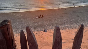 Una playa al atardecer con gente caminando y sentada sobre la arena.