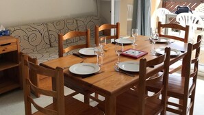 Un comedor con una mesa y sillas de madera, un televisor sobre un mueble bajo y vistas al exterior a través de una ventana.