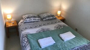 Una cama bien hecha con ropa de cama estampada, dos lámparas de noche y un cuadro colgado sobre la cama.