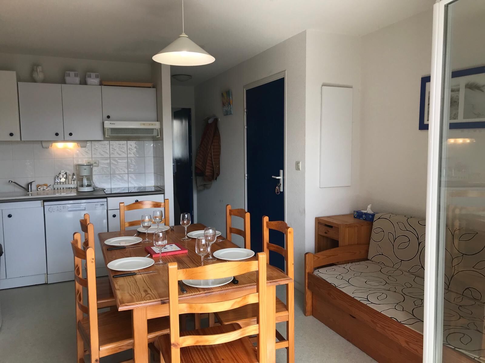 A compact kitchen with white cabinets, a dining table set for four, and a cozy seating area with a patterned cushion.