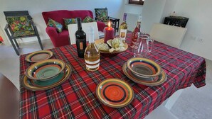 Une table à manger dressée avec des assiettes, des verres et des bouteilles, entourée de chaises et d’un canapé rouge.