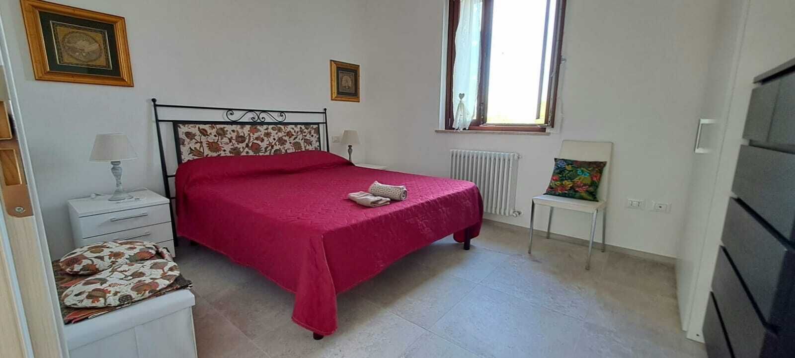 Un dormitorio con cama, mesitas de noche, radiador, ventana y televisor.