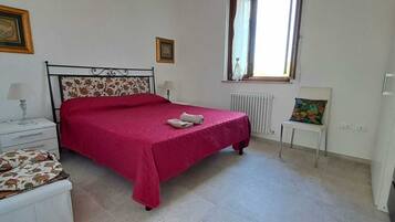 Un dormitorio con cama, mesitas de noche, radiador, ventana y televisor.