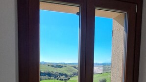 Une pièce dotée d’une grande fenêtre donnant sur un champ verdoyant et des collines lointaines.