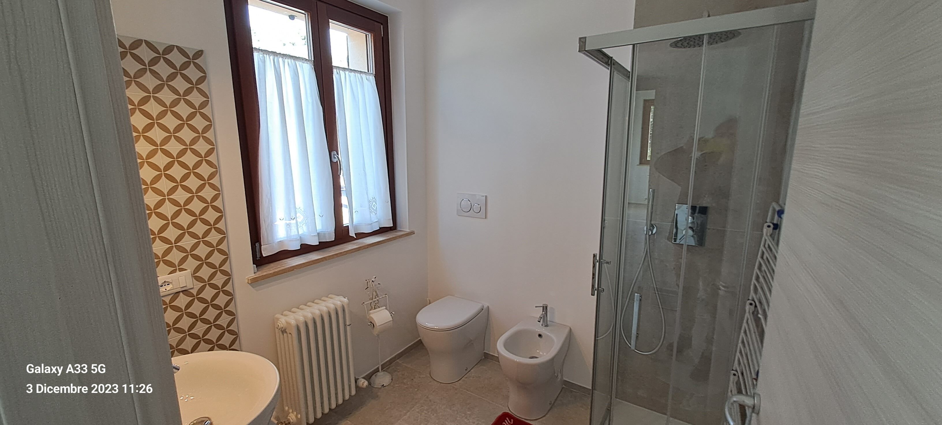 A bathroom with a toilet, bidet, radiator, and a glass shower enclosure.