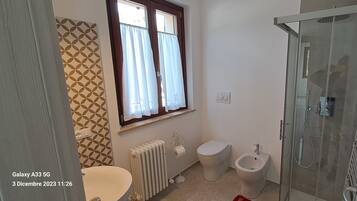 A bathroom with a toilet, bidet, radiator, and a glass shower enclosure.
