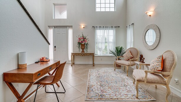 Een ruime woonkamer met een houten bureau, twee stoelen, een groot vloerkleed en een decoratieve spiegel.