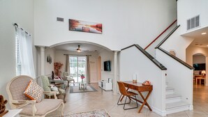 Een ruime woonkamer met een groot raam, een eethoek en een trap naar een hoger niveau.