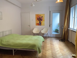 Une chambre à coucher avec un lit, deux chaises, une porte, une fenêtre et un tableau au mur.