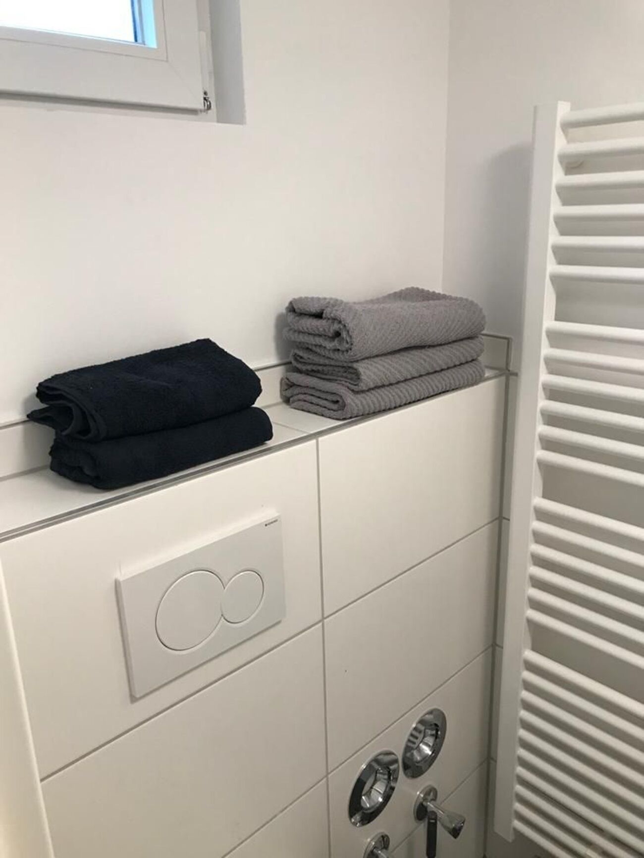 Un baño con un perchero con toallas dobladas, un panel de control con un botón circular y un radiador.