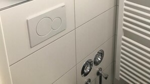 Une salle de bain avec un porte-serviettes où sont pliés les serviettes, un panneau de commande doté d’un bouton circulaire et un radiateur.