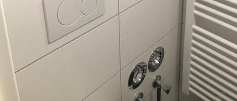 Un baño con un perchero con toallas dobladas, un panel de control con un botón circular y un radiador.