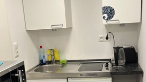 Une cuisine compacte avec des meubles blancs, un four à micro-ondes encastré, un évier et une machine à café.