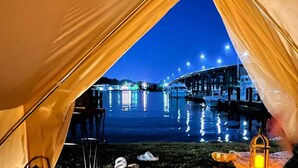 A tented area with a view of a water body and docked boats, under a night sky. - Dock, Dine, & Unwind: The Ultimate Waterfront Glamp Spot (Edgewater)