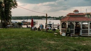 A gazebo with a red roof, a grassy area, and a dock with boats. - Dock, Dine, & Unwind: The Ultimate Waterfront Glamp Spot (Edgewater)