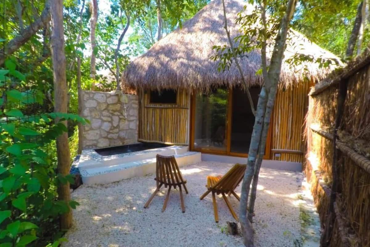 A thatched-roof hut with a stone wall, two wooden chairs, and a small outdoor seating area.