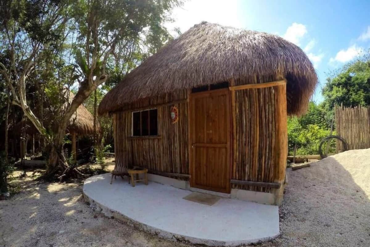 A rustic wooden hut with a thatched roof, a wooden door, and a small porch area.