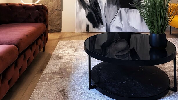 A modern living room with a large abstract painting, a tufted sofa, a round black coffee table, and a potted plant. - Private Parking• Stylish Elegance •King bed (Pittsburgh)