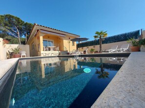 Une piscine aux eaux cristallines, entourée de chaises longues et d’un espace patio, le tout bordé d’un bâtiment jaune doté d’un toit en tuiles.