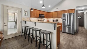 Une cuisine moderne avec des meubles en bois, un réfrigérateur en acier inoxydable, un four à micro-ondes et un coin bar avec des tabourets.