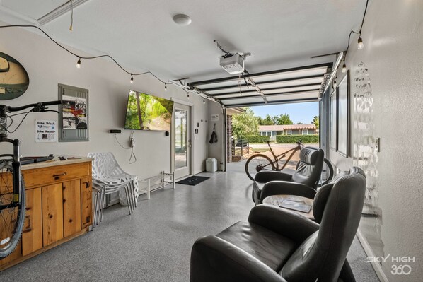 Habitación moderna y bien iluminada con una estación de reparación de bicicletas, zona de estar y grandes ventanales que ofrecen vistas al exterior.