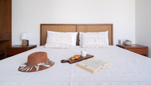 Un lit bien fait, avec une tête de lit en bois, deux oreillers, une table de chevet avec une lampe, une petite plante et un livre posé sur le lit.