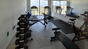 Une salle de sport moderne dotée de divers appareils d’exercice, de grandes fenêtres et offrant une vue sur le paysage urbain.