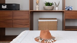 Une chambre à coucher bien rangée, avec un lit, une table de chevet sur laquelle se trouvent un livre, une tasse et un plateau avec deux biscuits. On y trouve également une armoire avec une tringle et une étagère où sont disposés des objets décoratifs.