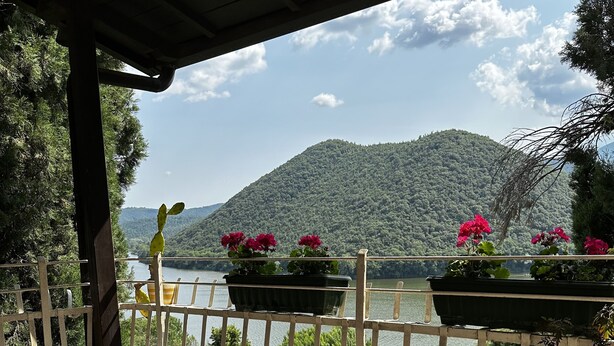 Een balkon met uitzicht op een meer en bergen, met plantenbakken en buitenmeubilair.