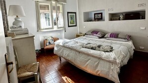 Een slaapkamer met een groot bed, een raam met zonwering, een nachtkastje en een stoel.