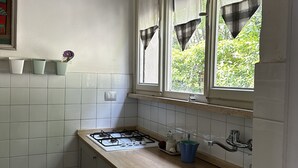 Een keuken met witte kastjes, een gasfornuis, een spoelbak en een raam met gordijnen.