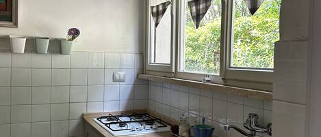 A kitchen with white cabinets, a gas stove, a sink, and a window with curtains.