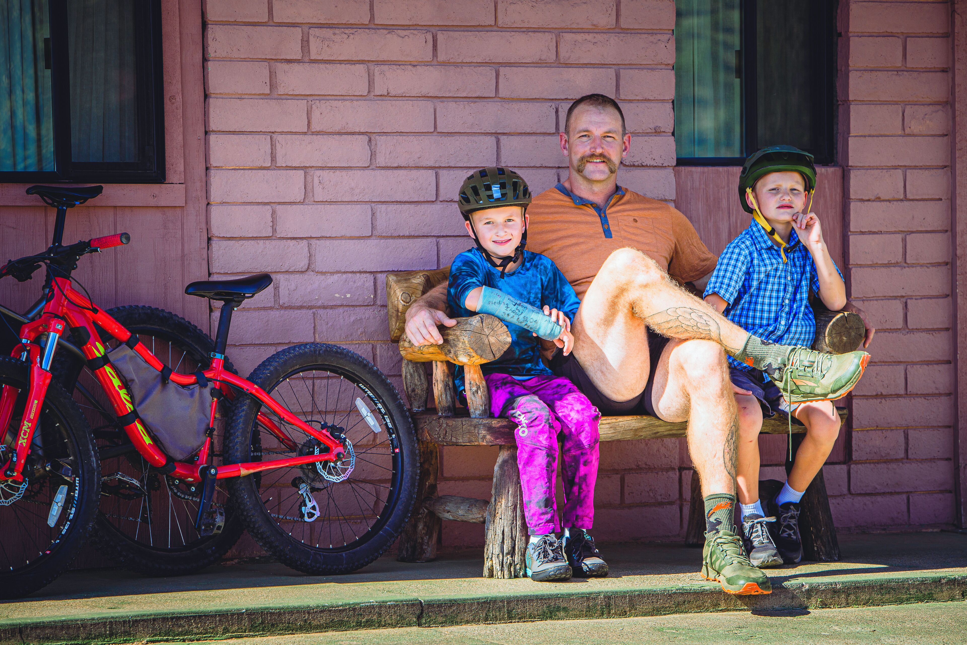 A man and two children sitting on a bench with a bicycle parked nearby.