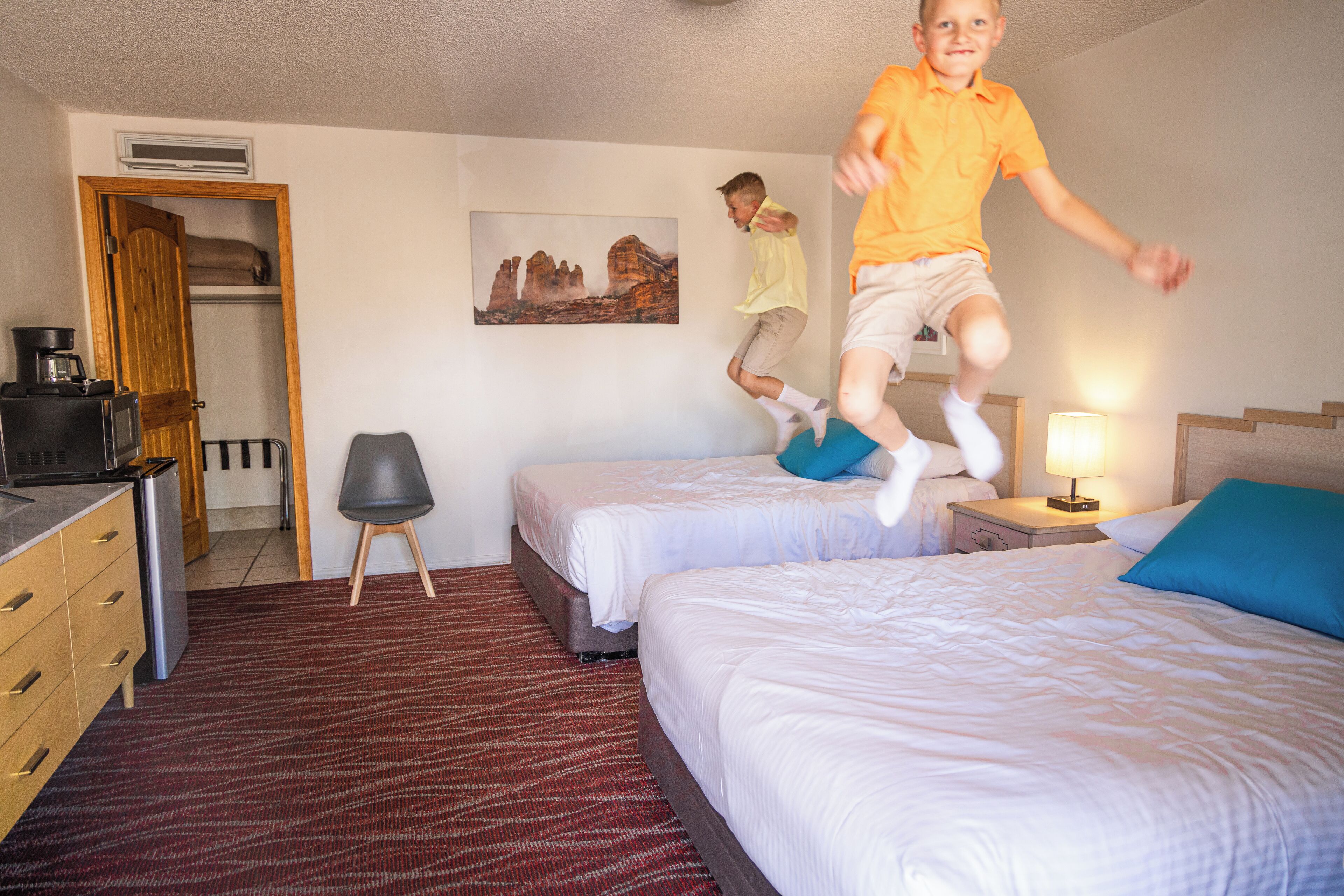 Een hotelkamer met twee bedden, een bureau met koffiezetapparaat, een stoel en een schilderij aan de muur.