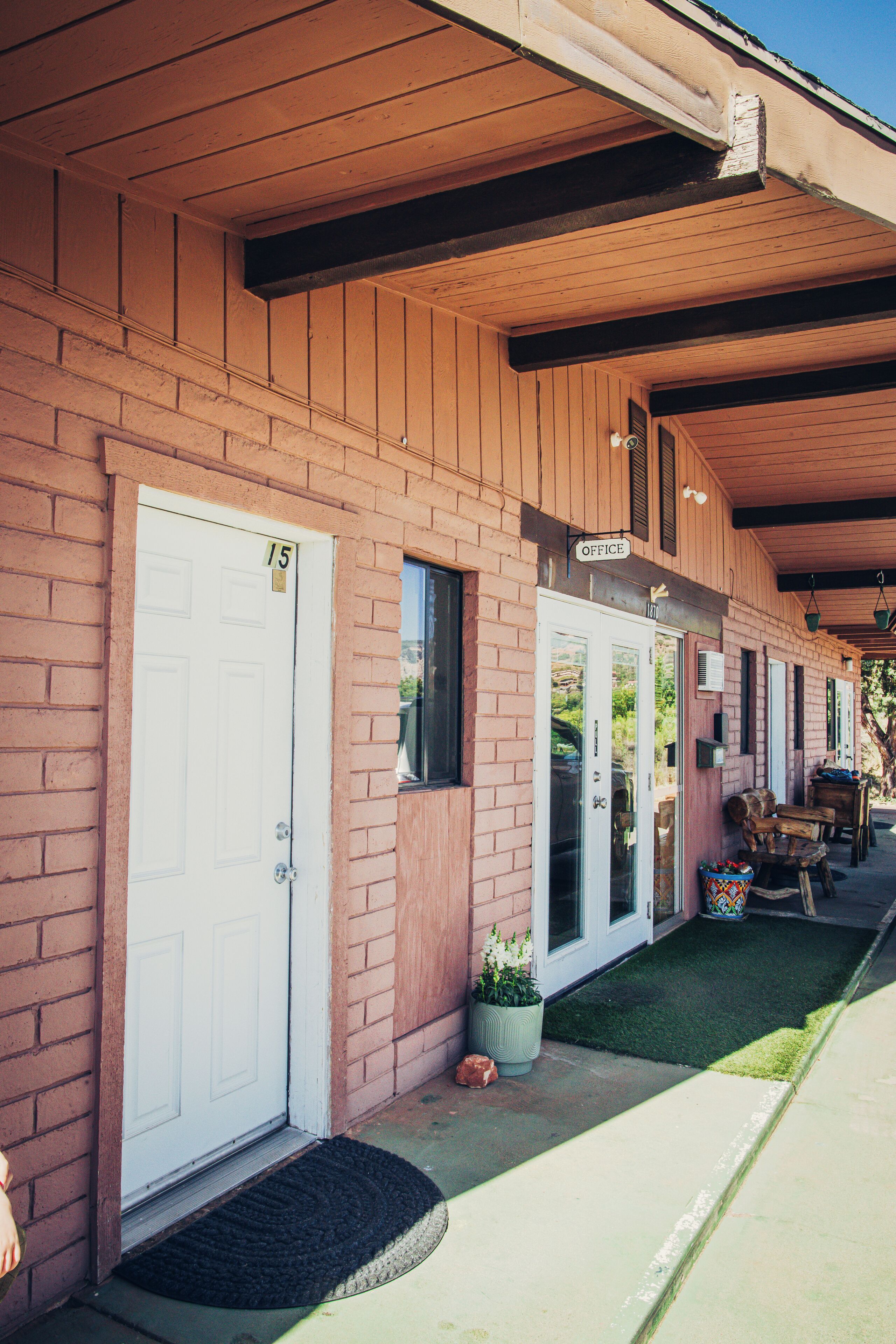 A row of single-story buildings with a brick facade, numbered doors, and a covered porch area.