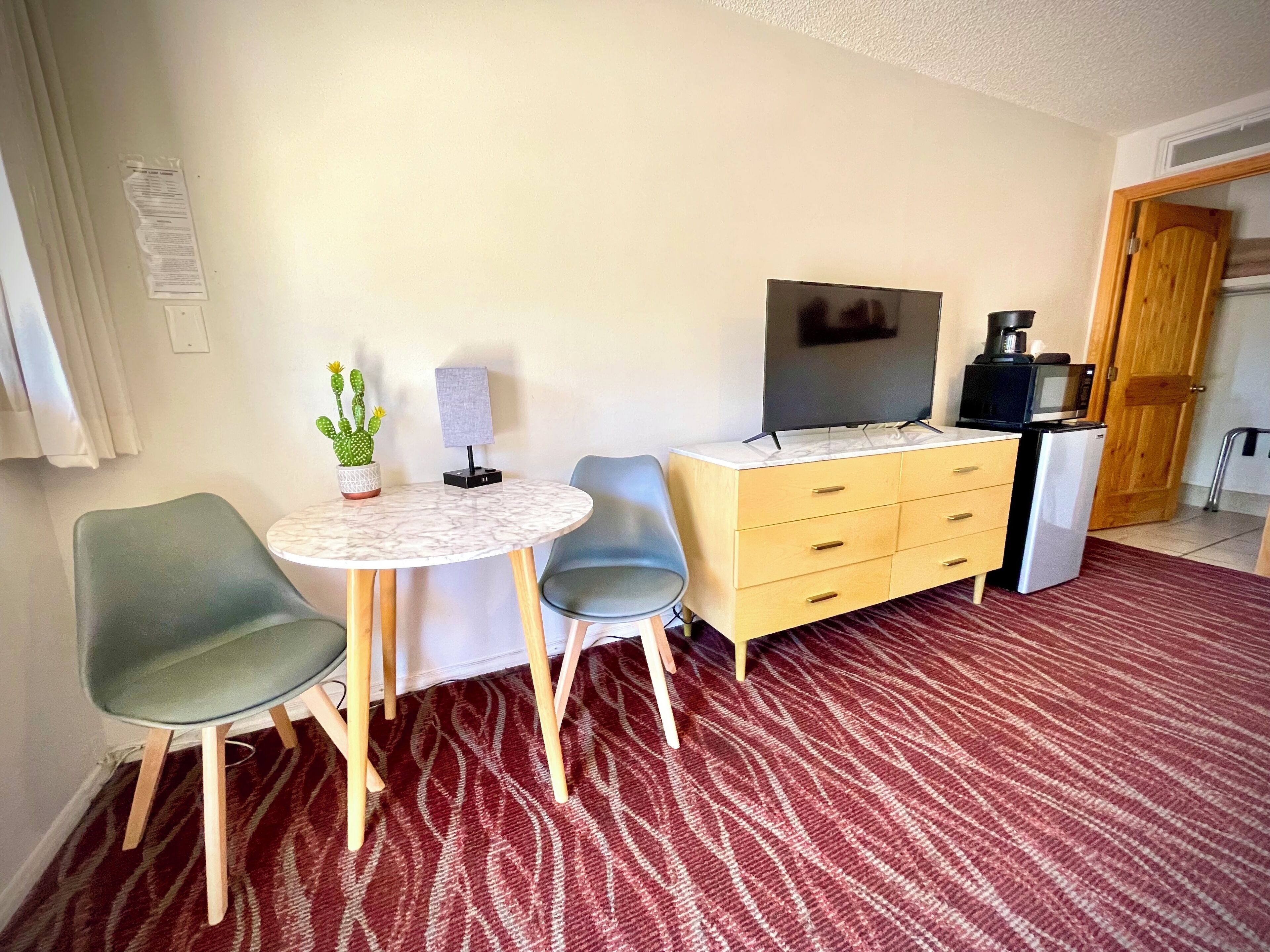 A compact room with a round table, two chairs, a TV, a microwave, and a small refrigerator.