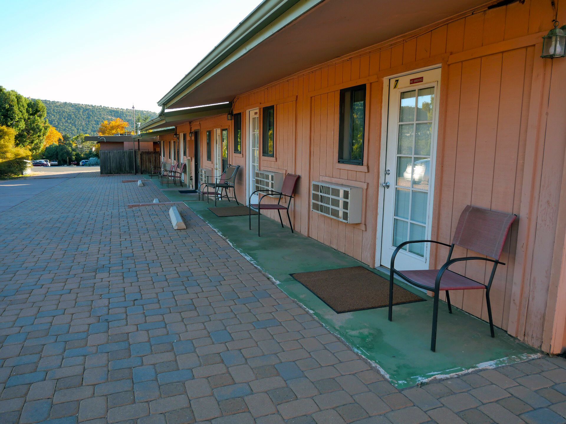 Un motel con estacionamiento de adoquines y una hilera de habitaciones con entradas individuales.
