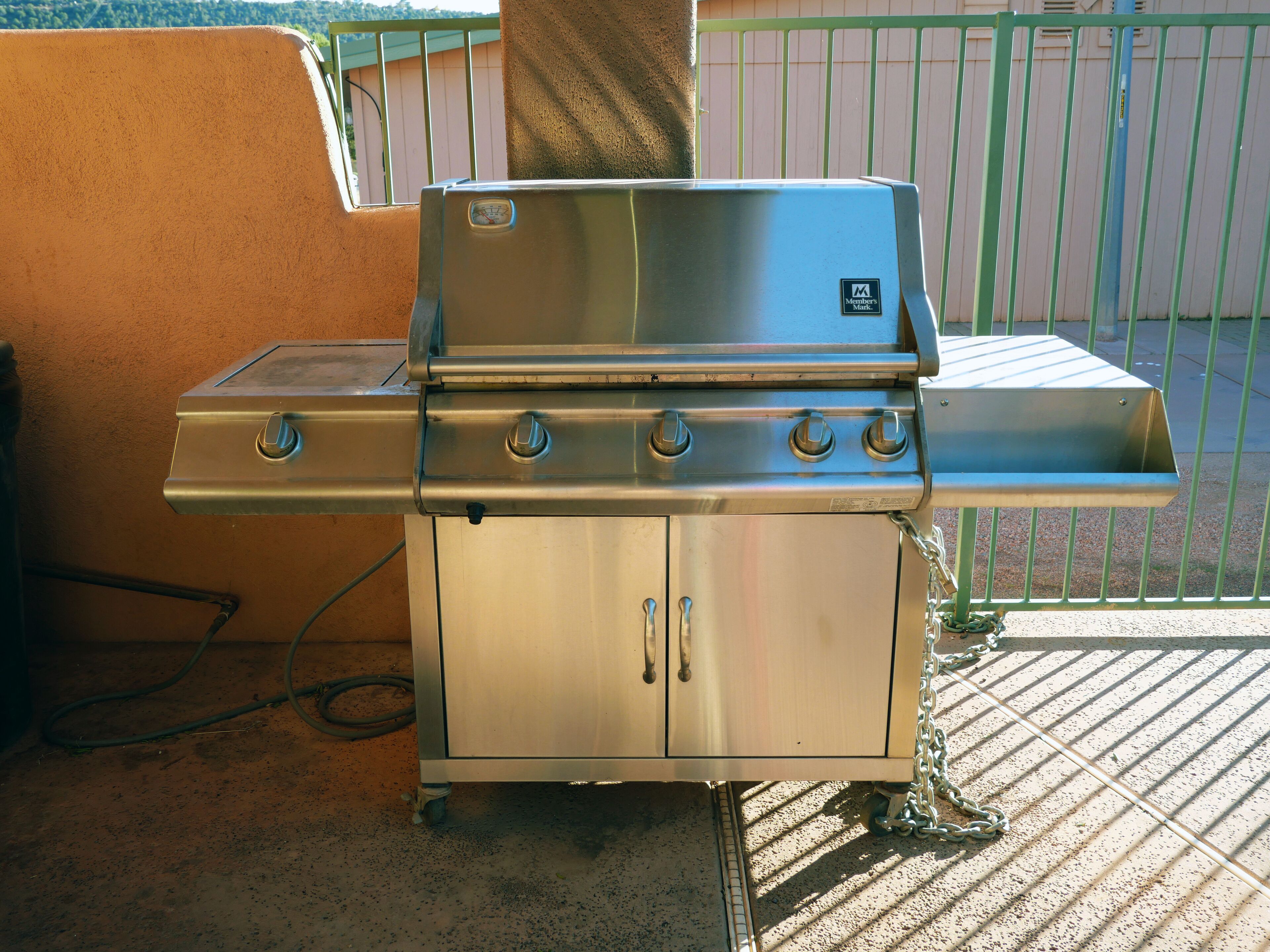 En grill i rustfrit stål med fire brændere og en hylde, placeret på en beton terrasse.