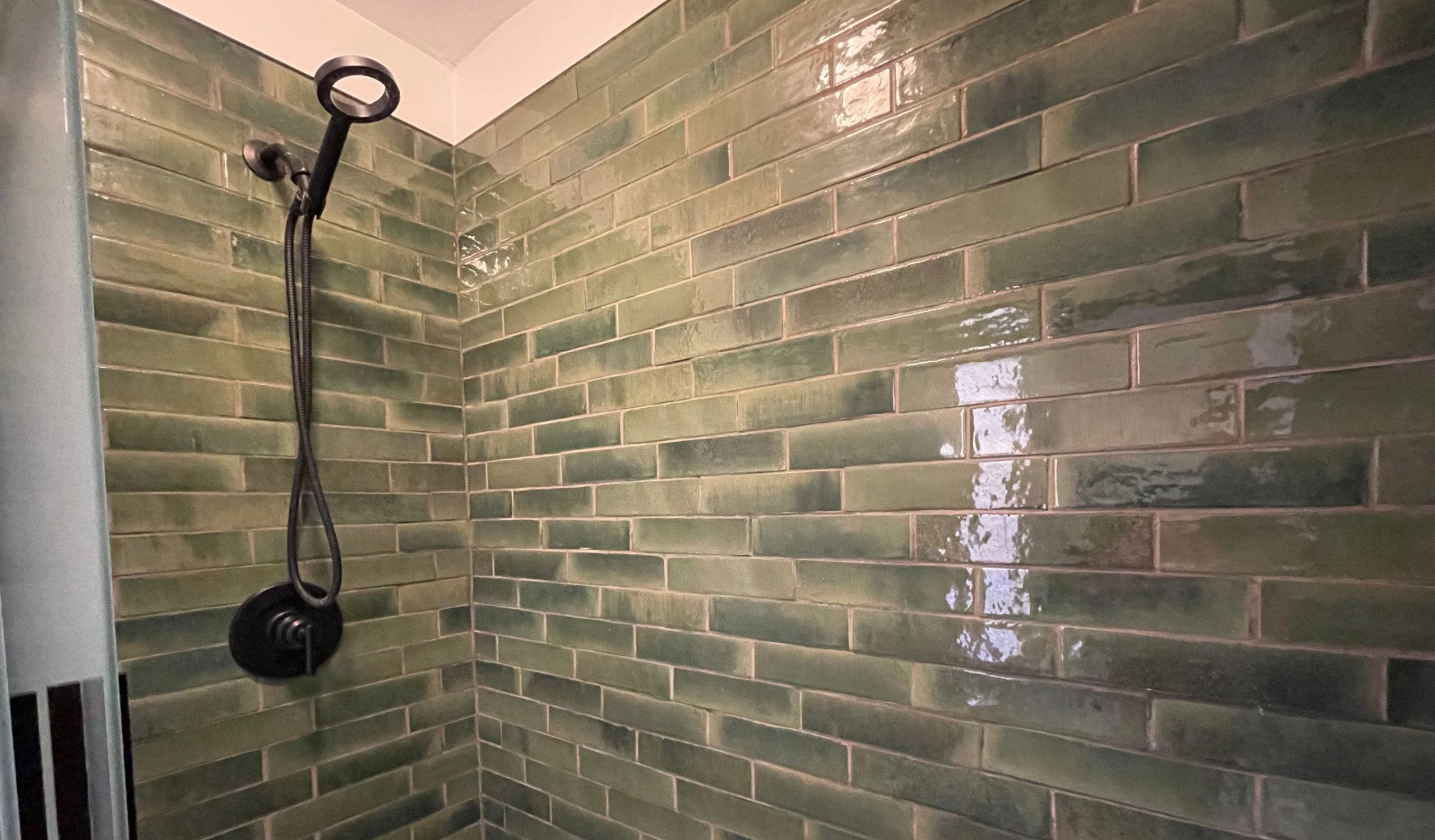 A bathroom with green mosaic tiles and a shower with a black hose.