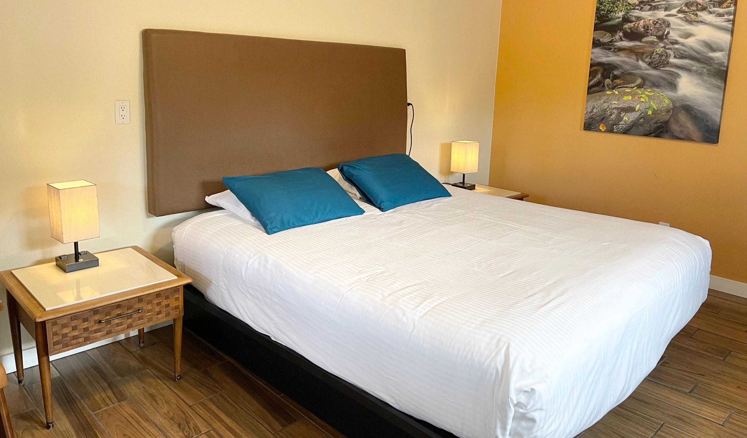 Habitación de hotel con una cama grande, dos lámparas de noche, una mesita de noche de madera y un cuadro en la pared.