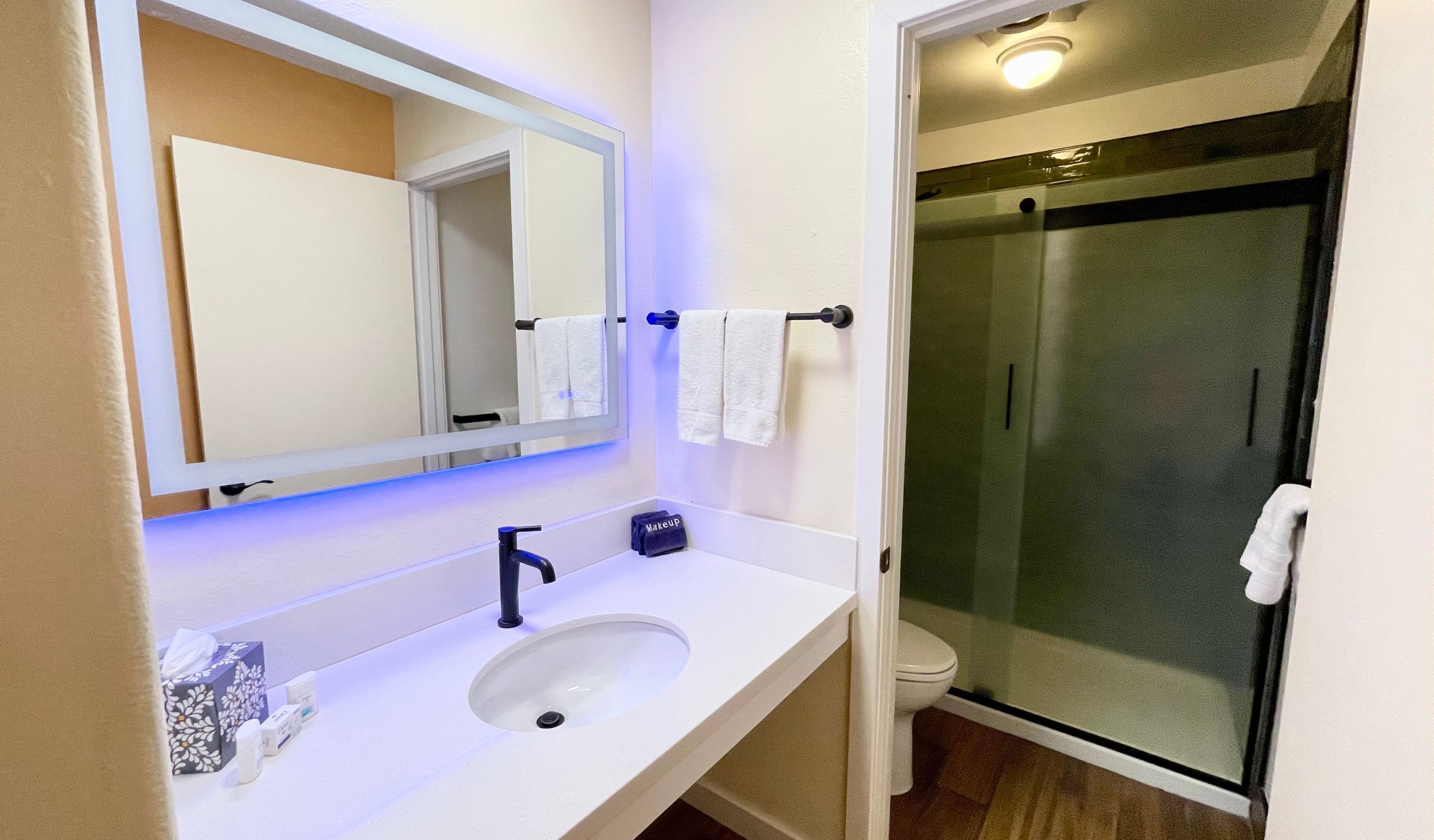 Un baño con lavamanos blanco, espejo, toallero y cabina de ducha con mampara de vidrio.