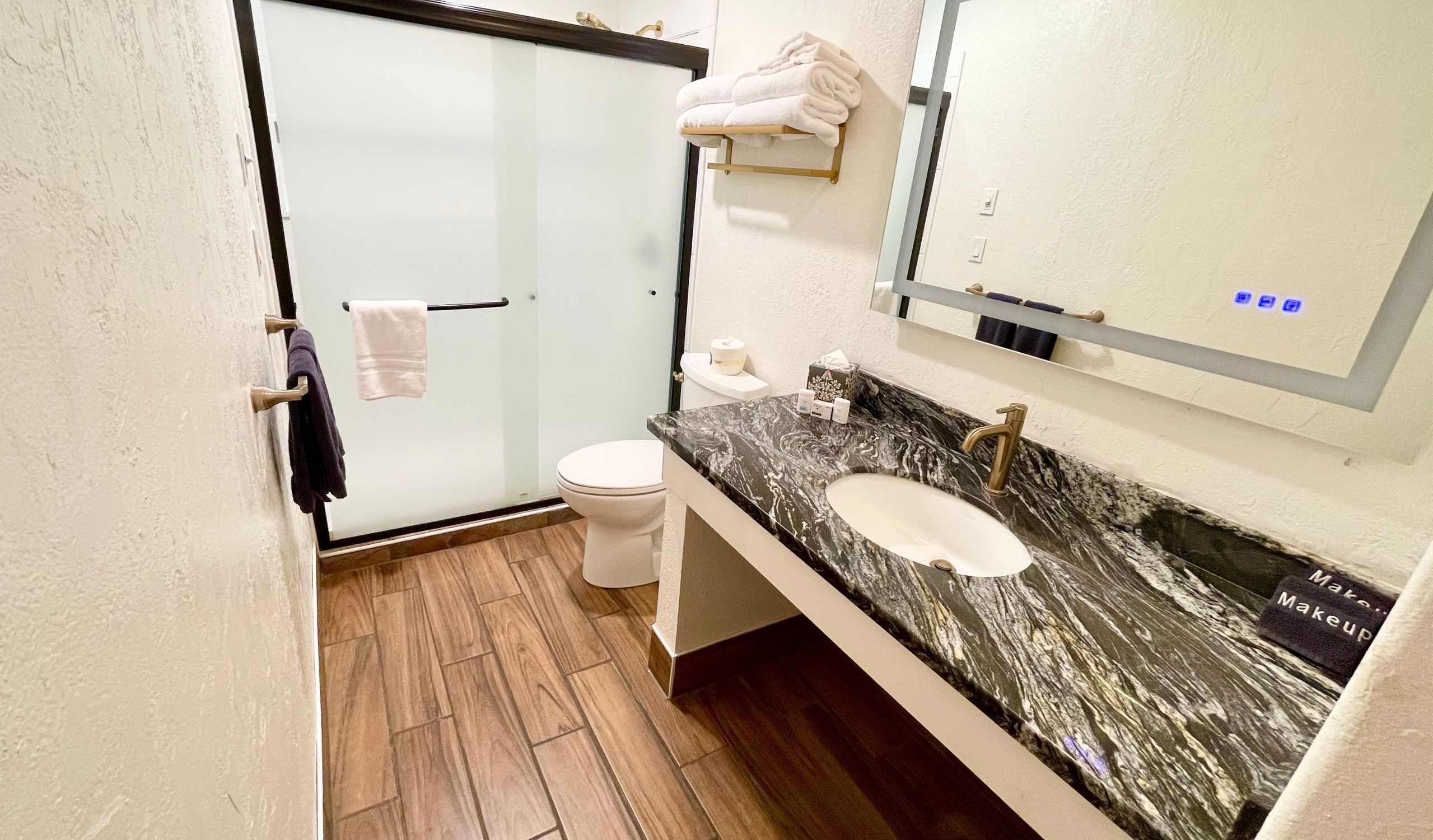 Une salle de bain avec une douche à porte en verre, des toilettes blanches, un lavabo en marbre et un porte-serviettes.