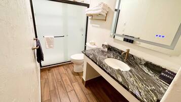 Une salle de bain avec une douche à porte en verre, des toilettes blanches, un lavabo en marbre et un porte-serviettes.