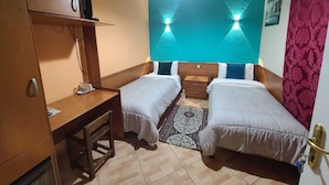 Una habitación compacta con dos camas individuales, un escritorio con silla, una mesita y un televisor montado en la pared.