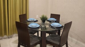 Un comedor con una mesa redonda de vidrio, sillas de madera oscura y platos azules.