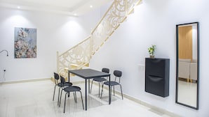A modern interior with a staircase, a dining area with chairs and a table, a wall-mounted TV, and a painting. - Badrani A - Qaswarah Residence  (Madinah)